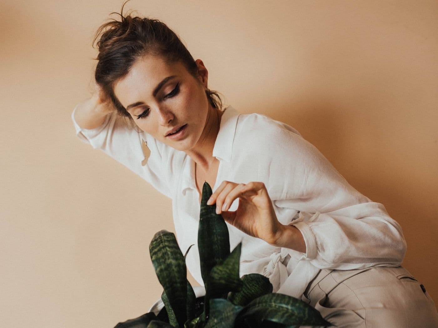 Model in an ivory outfit holding a green plant